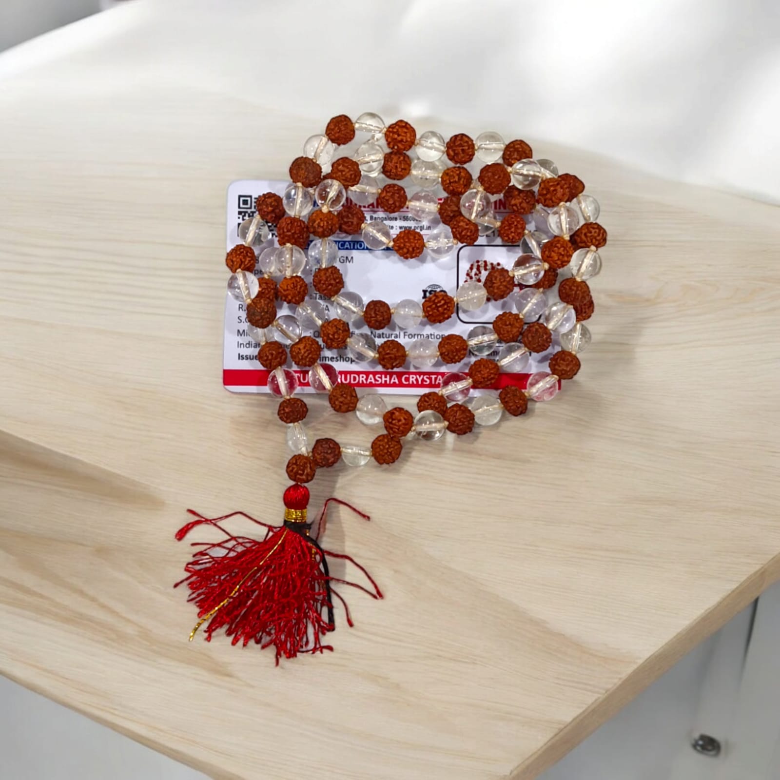 A beautiful Rudraksha and Sphatik Crystal Mala with natural beads, arranged neatly, available in 27+1 and 108+1 variants, displayed on a spiritual-themed background