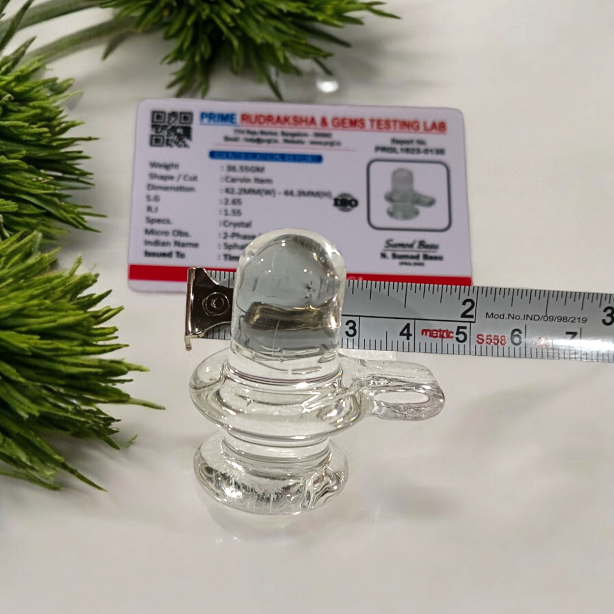A clear, polished Sphatik (Crystal) Shivling placed on a small round base, intricately designed with fine details. The Shivling radiates purity and divine energy, symbolizing Lord Shiva. Ideal for worship, this lab-certified Sphatik Shivling from Timeshopee adds a spiritual touch to your home or temple setting.