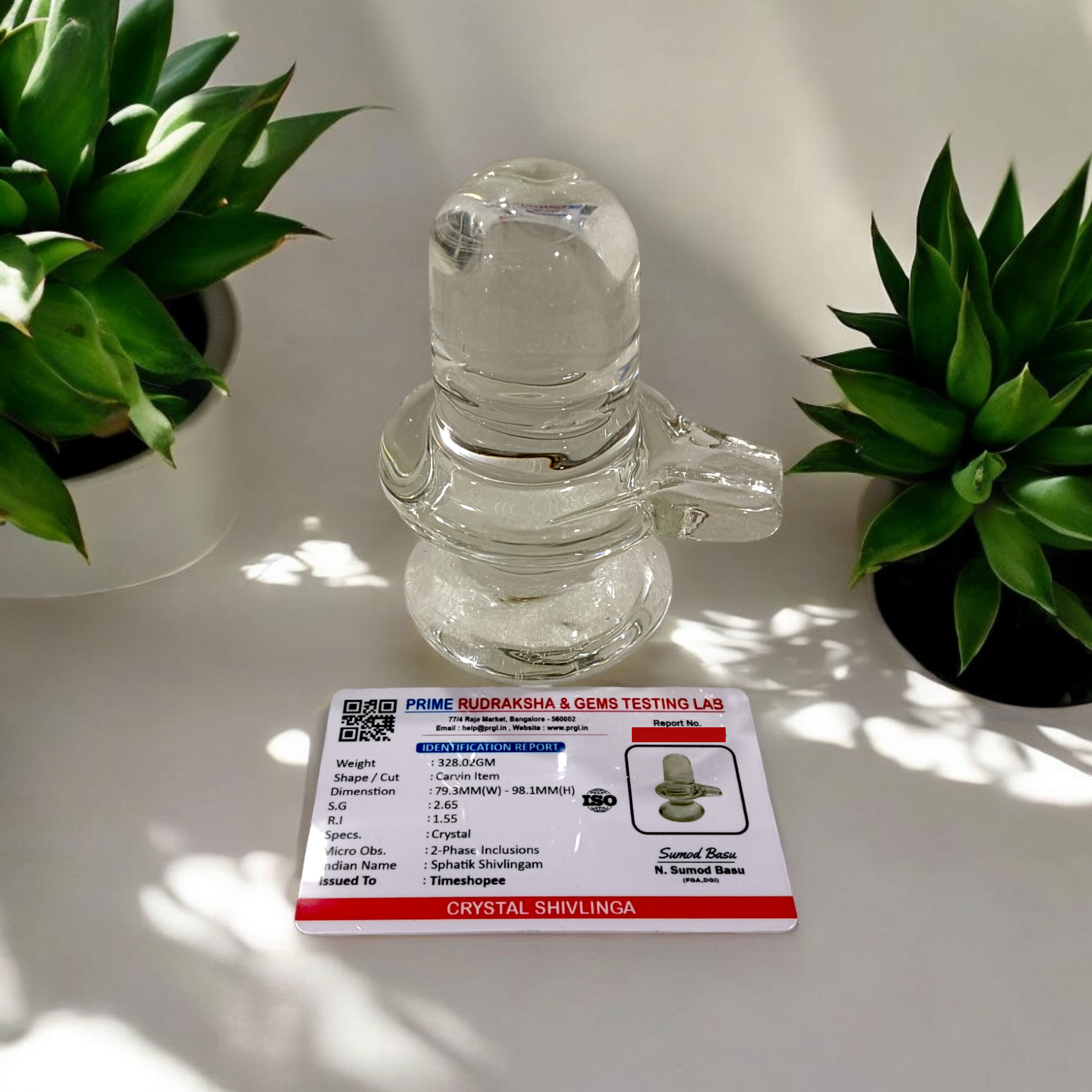 A clear, polished Sphatik (Crystal) Shivling placed on a small round base, intricately designed with fine details. The Shivling radiates purity and divine energy, symbolizing Lord Shiva. Ideal for worship, this lab-certified Sphatik Shivling from Timeshopee adds a spiritual touch to your home or temple setting.