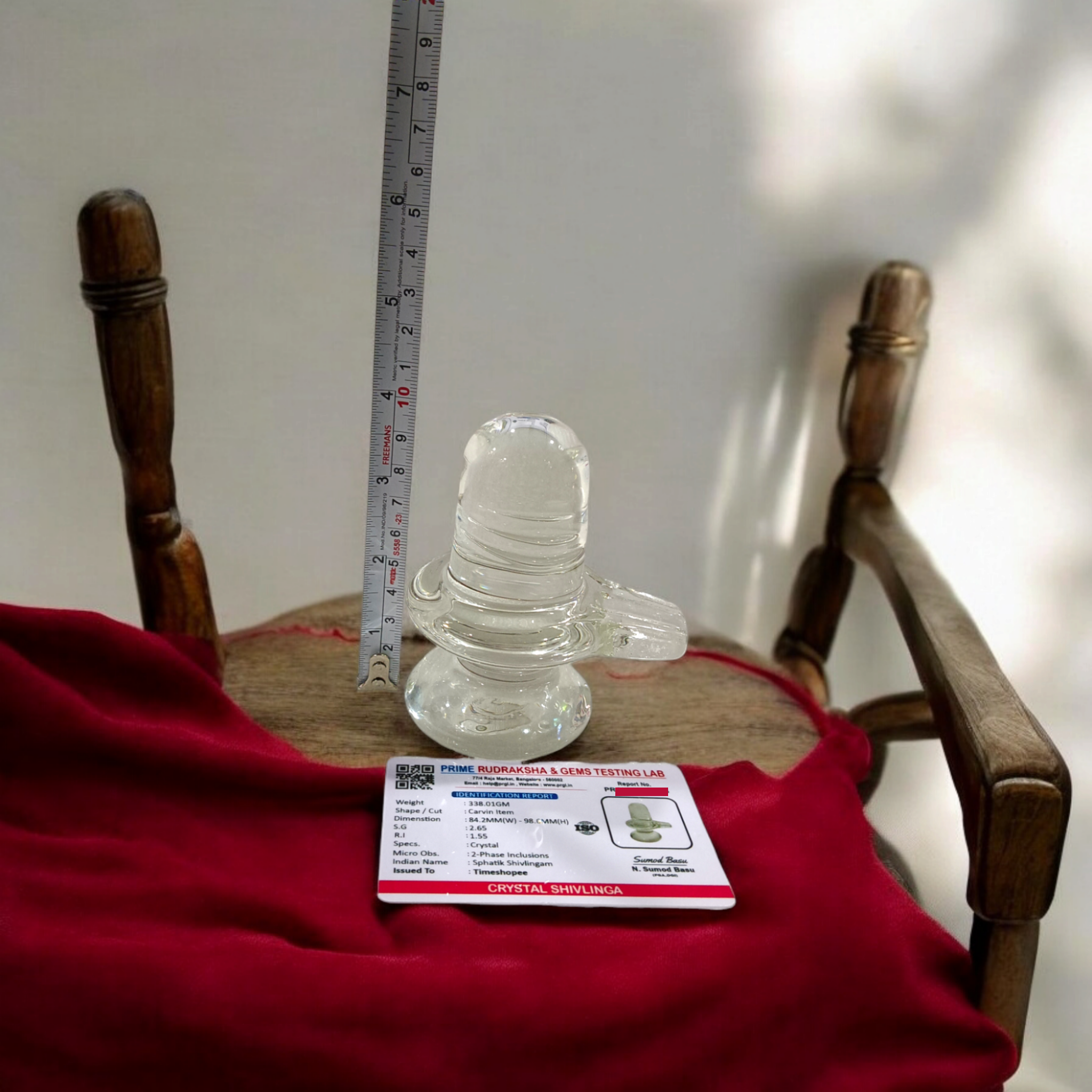 A clear, polished Sphatik (Crystal) Shivling placed on a small round base, intricately designed with fine details. The Shivling radiates purity and divine energy, symbolizing Lord Shiva. Ideal for worship, this lab-certified Sphatik Shivling from Timeshopee adds a spiritual touch to your home or temple setting.