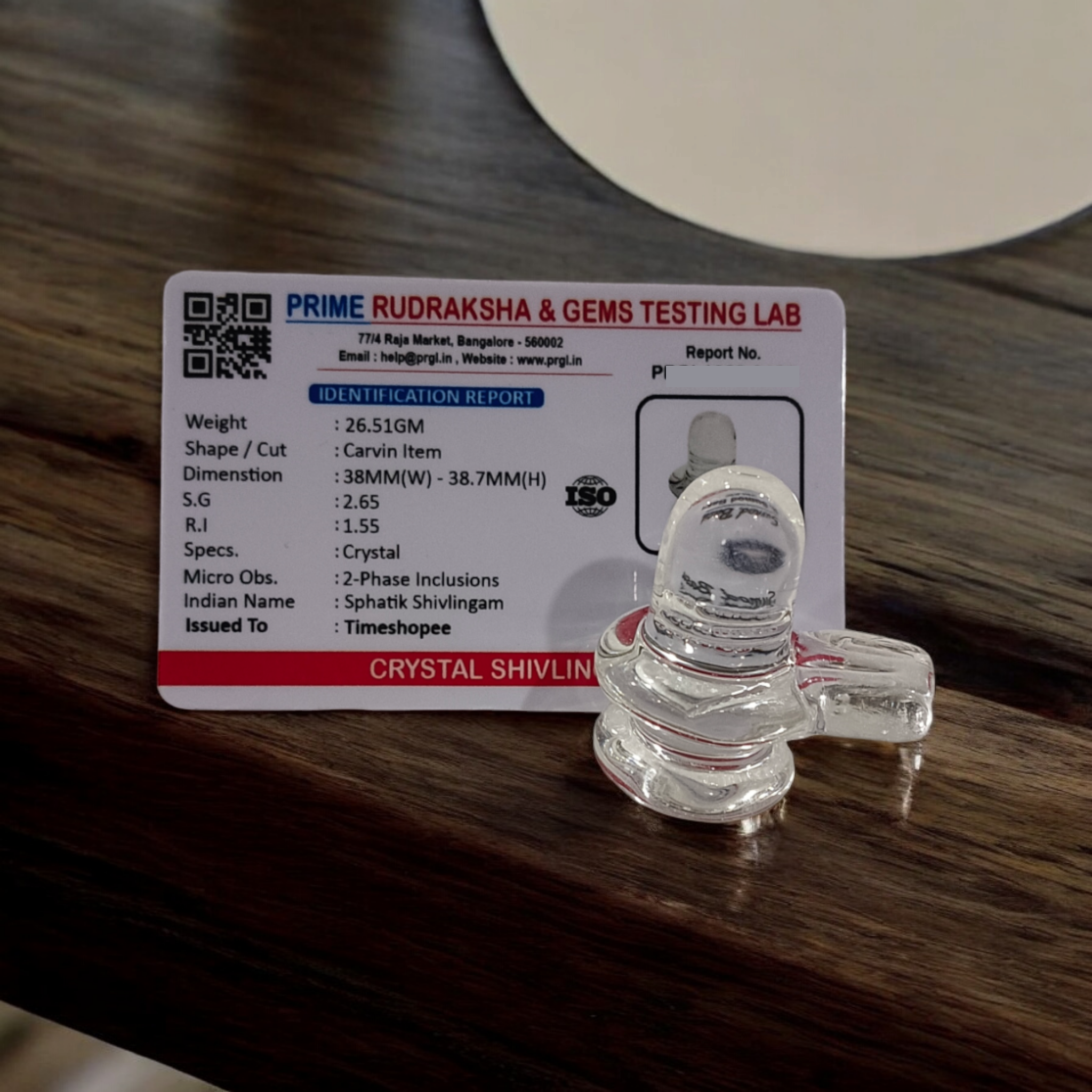 A clear, polished Sphatik (Crystal) Shivling placed on a small round base, intricately designed with fine details. The Shivling radiates purity and divine energy, symbolizing Lord Shiva. Ideal for worship, this lab-certified Sphatik Shivling from Timeshopee adds a spiritual touch to your home or temple setting.