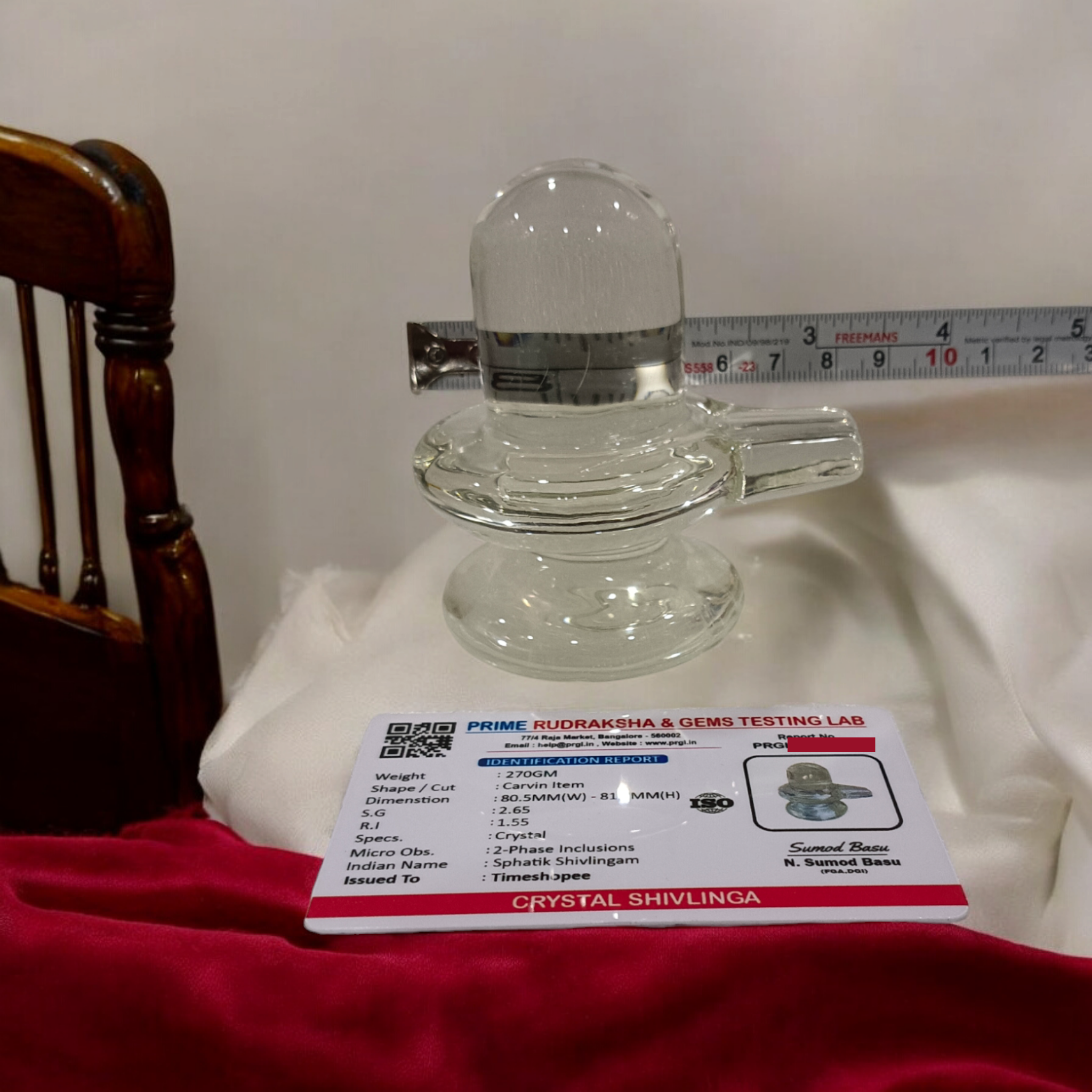 A clear, polished Sphatik (Crystal) Shivling placed on a small round base, intricately designed with fine details. The Shivling radiates purity and divine energy, symbolizing Lord Shiva. Ideal for worship, this lab-certified Sphatik Shivling from Timeshopee adds a spiritual touch to your home or temple setting.