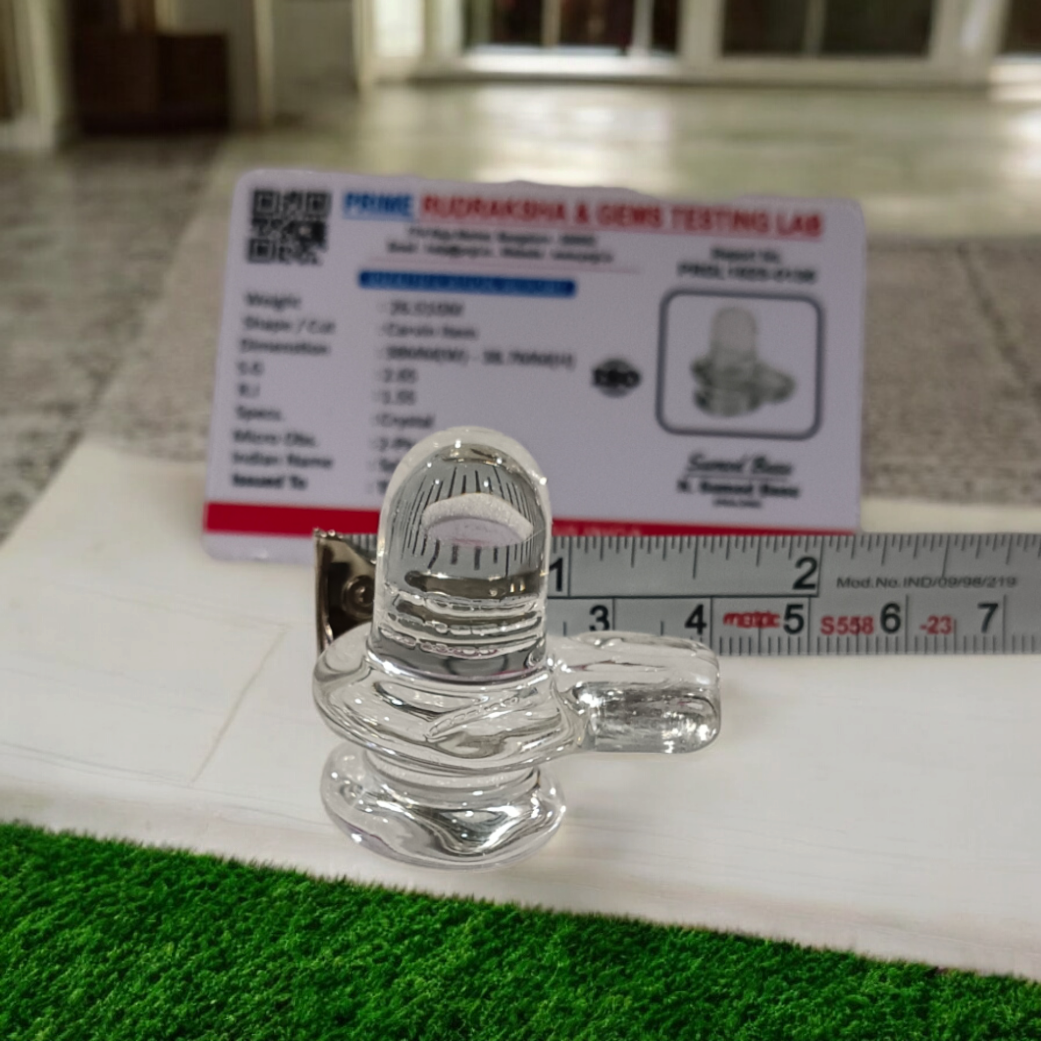 A clear, polished Sphatik (Crystal) Shivling placed on a small round base, intricately designed with fine details. The Shivling radiates purity and divine energy, symbolizing Lord Shiva. Ideal for worship, this lab-certified Sphatik Shivling from Timeshopee adds a spiritual touch to your home or temple setting.