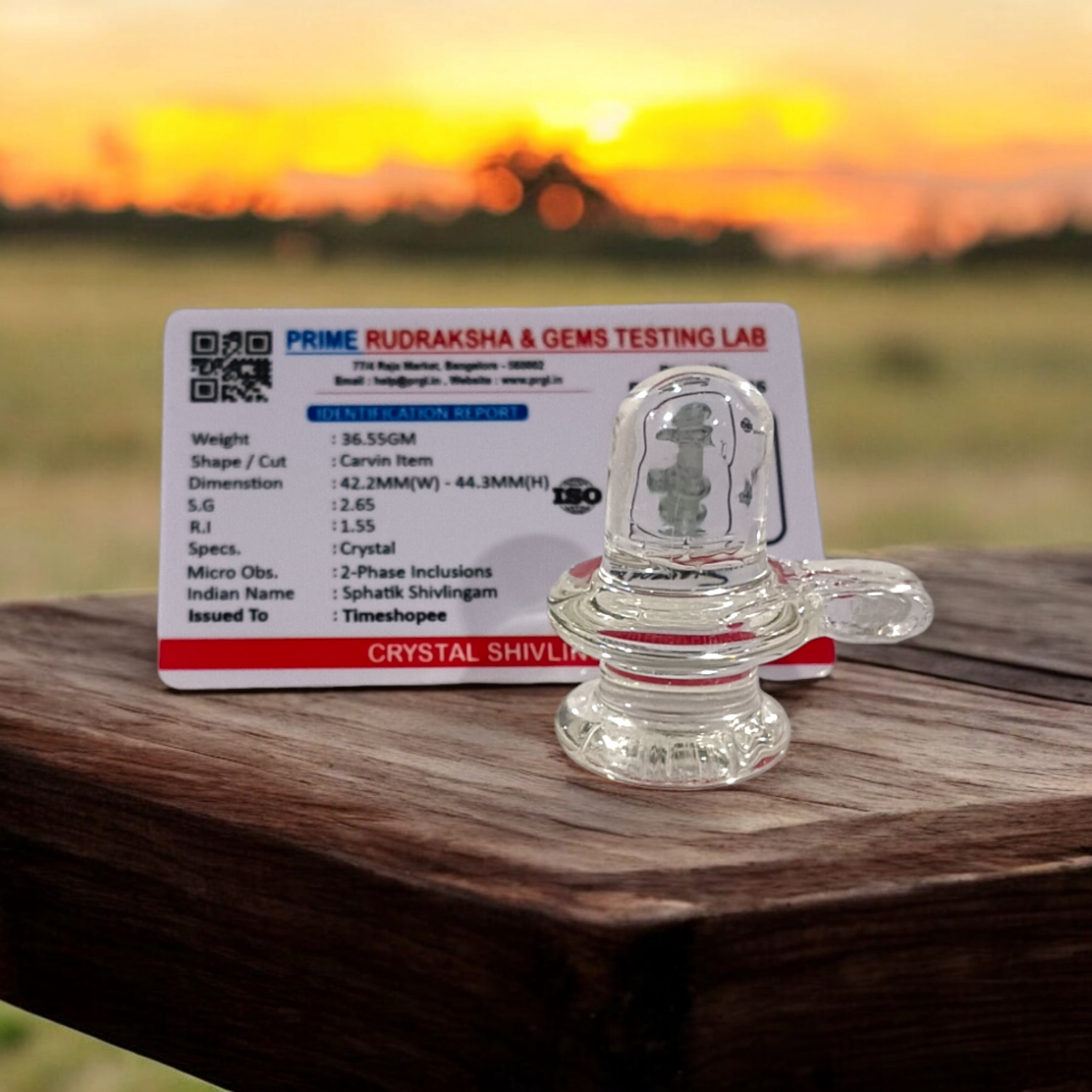 A clear, polished Sphatik (Crystal) Shivling placed on a small round base, intricately designed with fine details. The Shivling radiates purity and divine energy, symbolizing Lord Shiva. Ideal for worship, this lab-certified Sphatik Shivling from Timeshopee adds a spiritual touch to your home or temple setting.