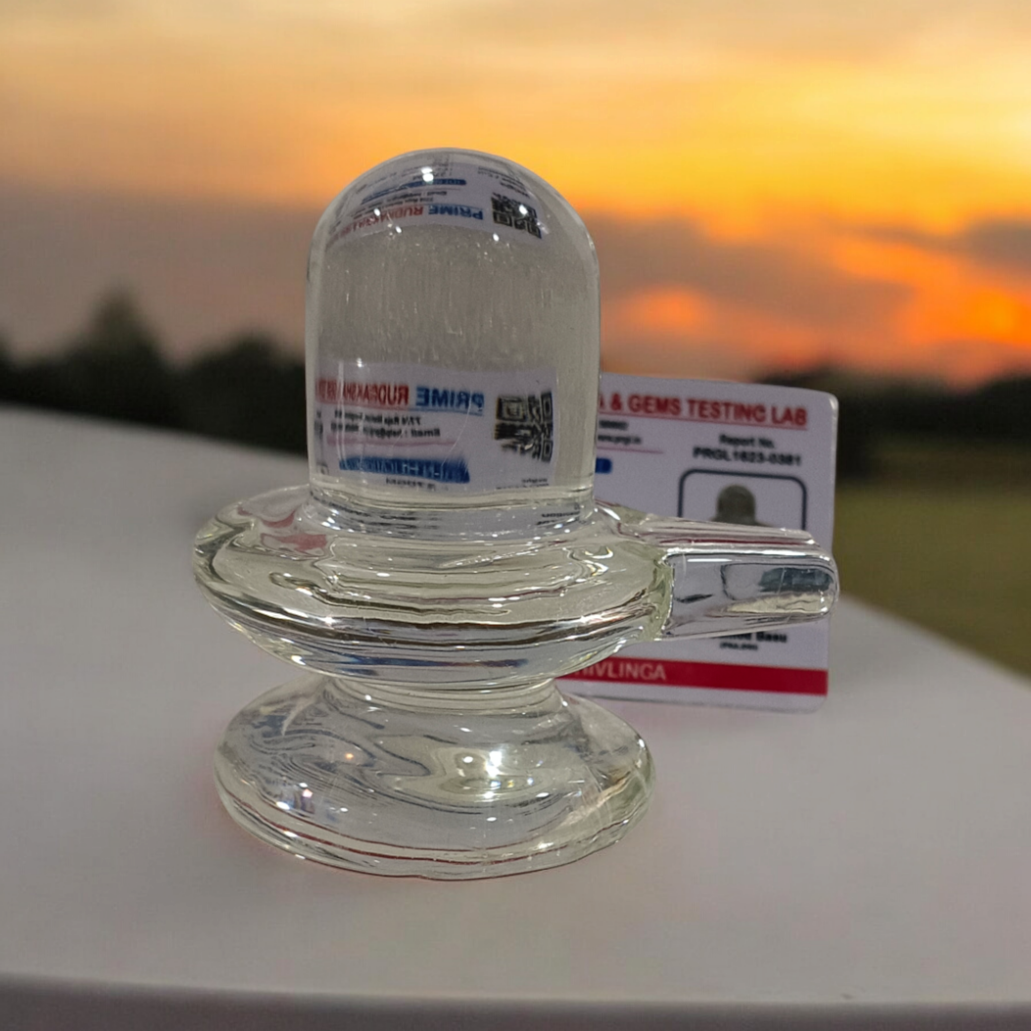 A clear, polished Sphatik (Crystal) Shivling placed on a small round base, intricately designed with fine details. The Shivling radiates purity and divine energy, symbolizing Lord Shiva. Ideal for worship, this lab-certified Sphatik Shivling from Timeshopee adds a spiritual touch to your home or temple setting.