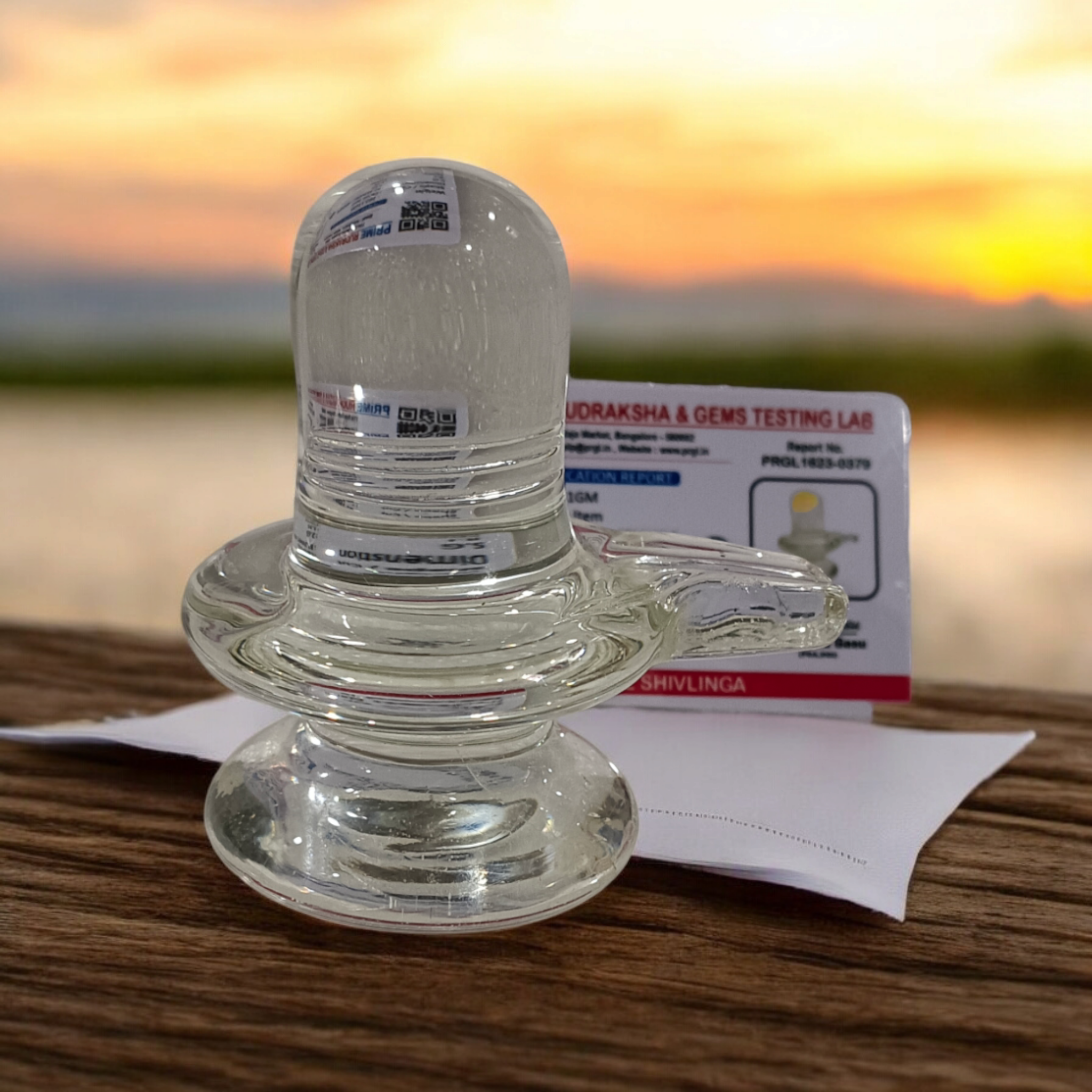 A clear, polished Sphatik (Crystal) Shivling placed on a small round base, intricately designed with fine details. The Shivling radiates purity and divine energy, symbolizing Lord Shiva. Ideal for worship, this lab-certified Sphatik Shivling from Timeshopee adds a spiritual touch to your home or temple setting.