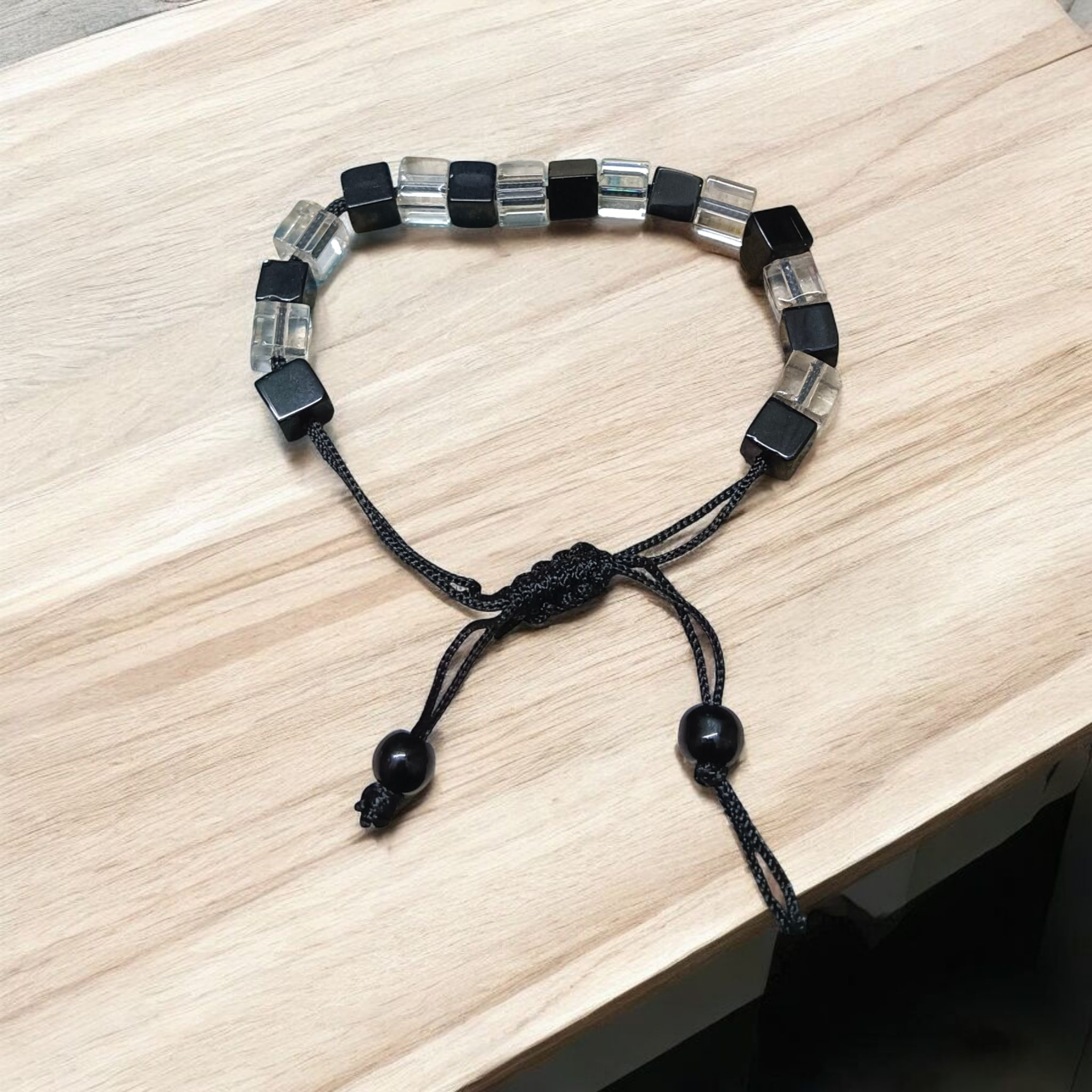 Black and white crystal bracelet with an evil eye symbol, featuring an adjustable thread for a customizable fit, designed for attraction and protection.