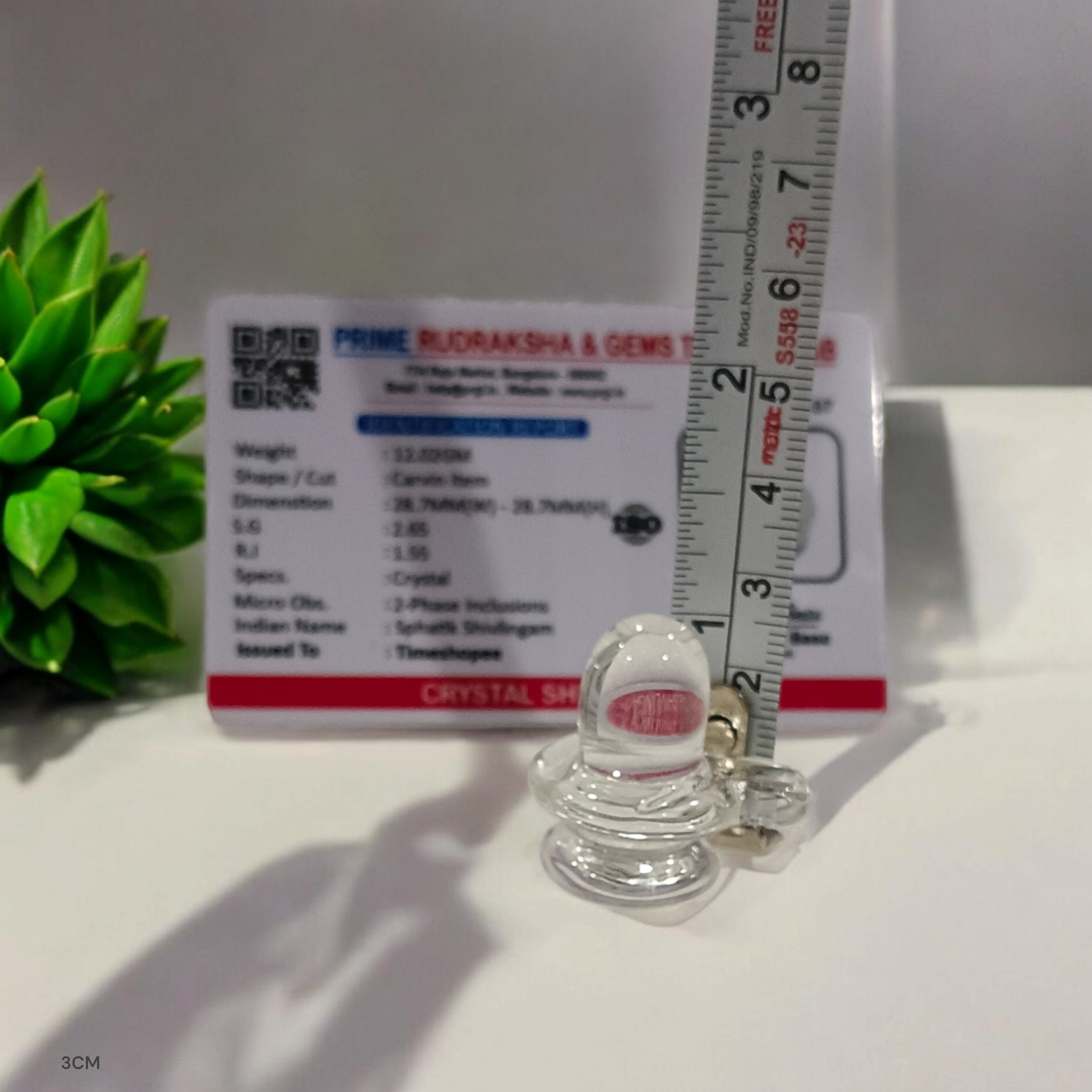 A clear, polished Sphatik (Crystal) Shivling placed on a small round base, intricately designed with fine details. The Shivling radiates purity and divine energy, symbolizing Lord Shiva. Ideal for worship, this lab-certified Sphatik Shivling from Timeshopee adds a spiritual touch to your home or temple setting.