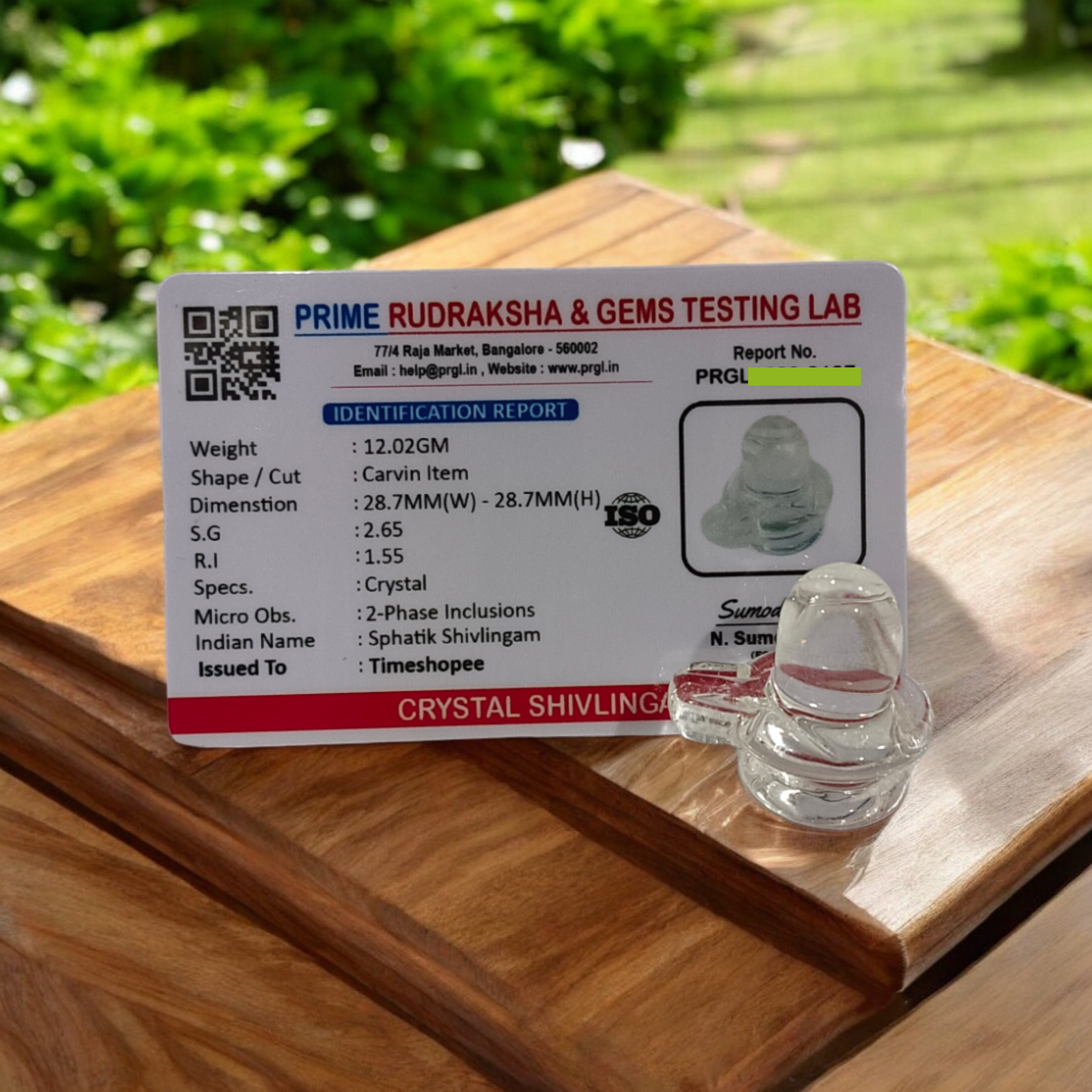A clear, polished Sphatik (Crystal) Shivling placed on a small round base, intricately designed with fine details. The Shivling radiates purity and divine energy, symbolizing Lord Shiva. Ideal for worship, this lab-certified Sphatik Shivling from Timeshopee adds a spiritual touch to your home or temple setting.