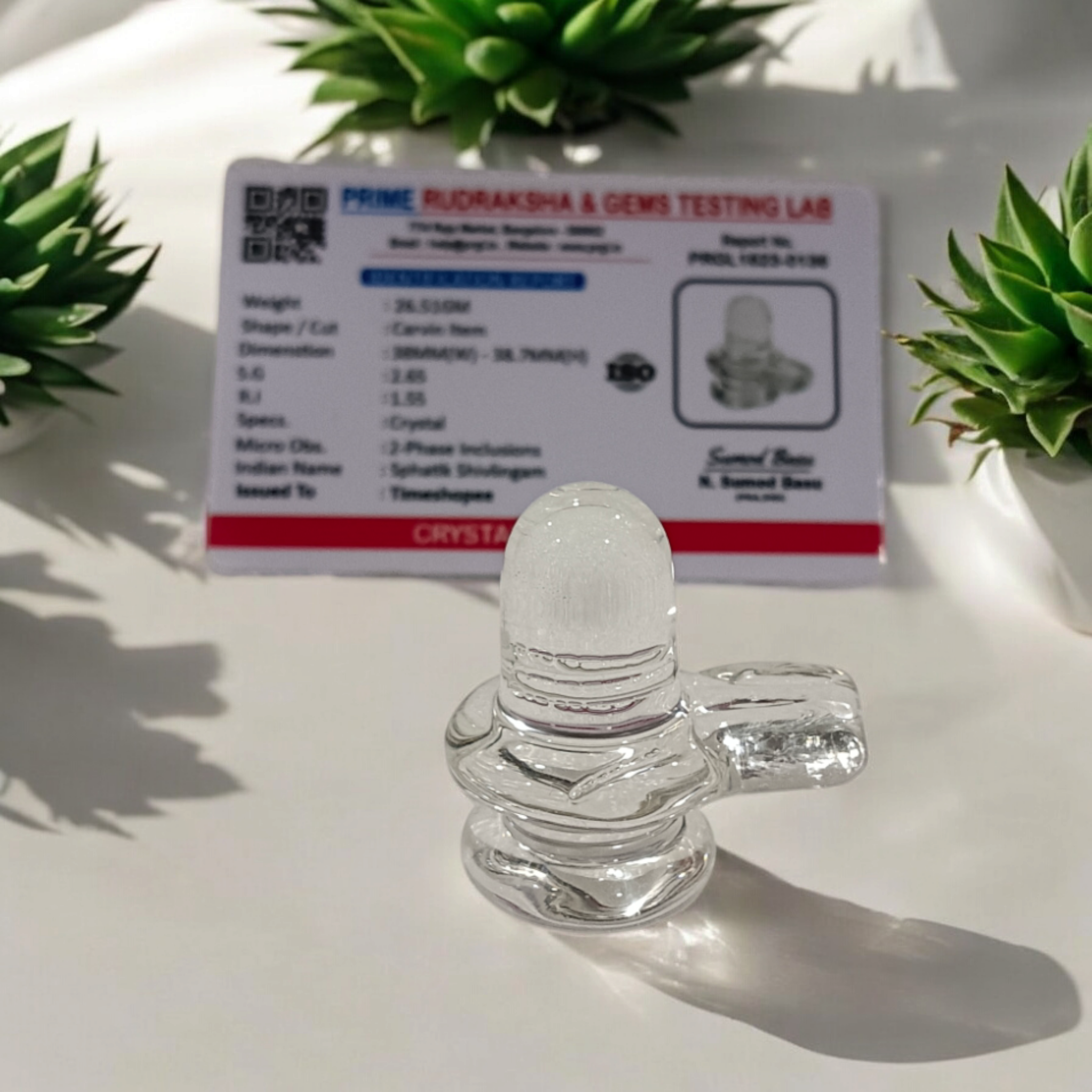 A clear, polished Sphatik (Crystal) Shivling placed on a small round base, intricately designed with fine details. The Shivling radiates purity and divine energy, symbolizing Lord Shiva. Ideal for worship, this lab-certified Sphatik Shivling from Timeshopee adds a spiritual touch to your home or temple setting.