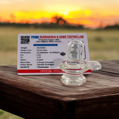 A clear, polished Sphatik (Crystal) Shivling placed on a small round base, intricately designed with fine details. The Shivling radiates purity and divine energy, symbolizing Lord Shiva. Ideal for worship, this lab-certified Sphatik Shivling from Timeshopee adds a spiritual touch to your home or temple setting.