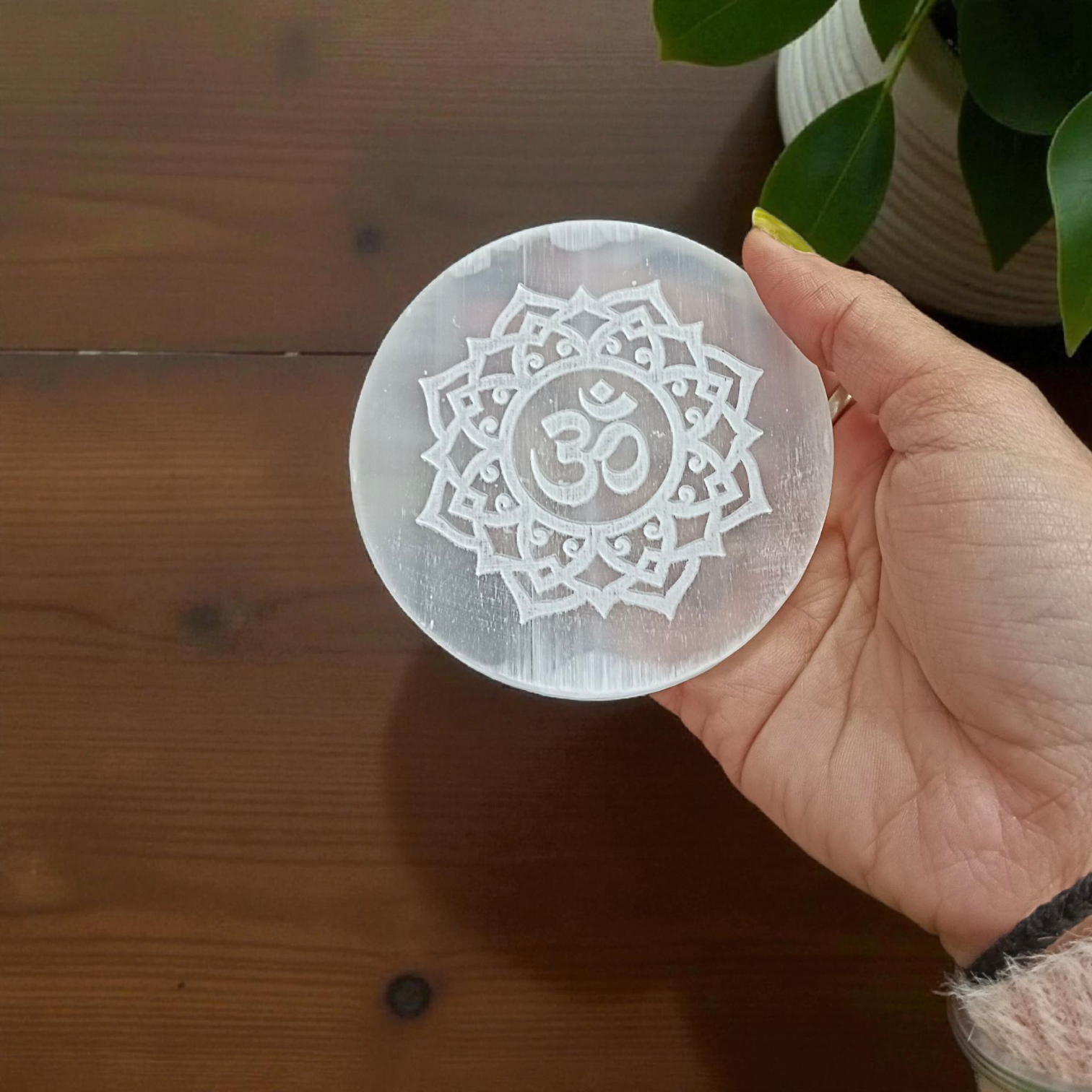 A polished round Selenite charging plate featuring a carved Om symbol, used for pooja, décor, and energy cleansing