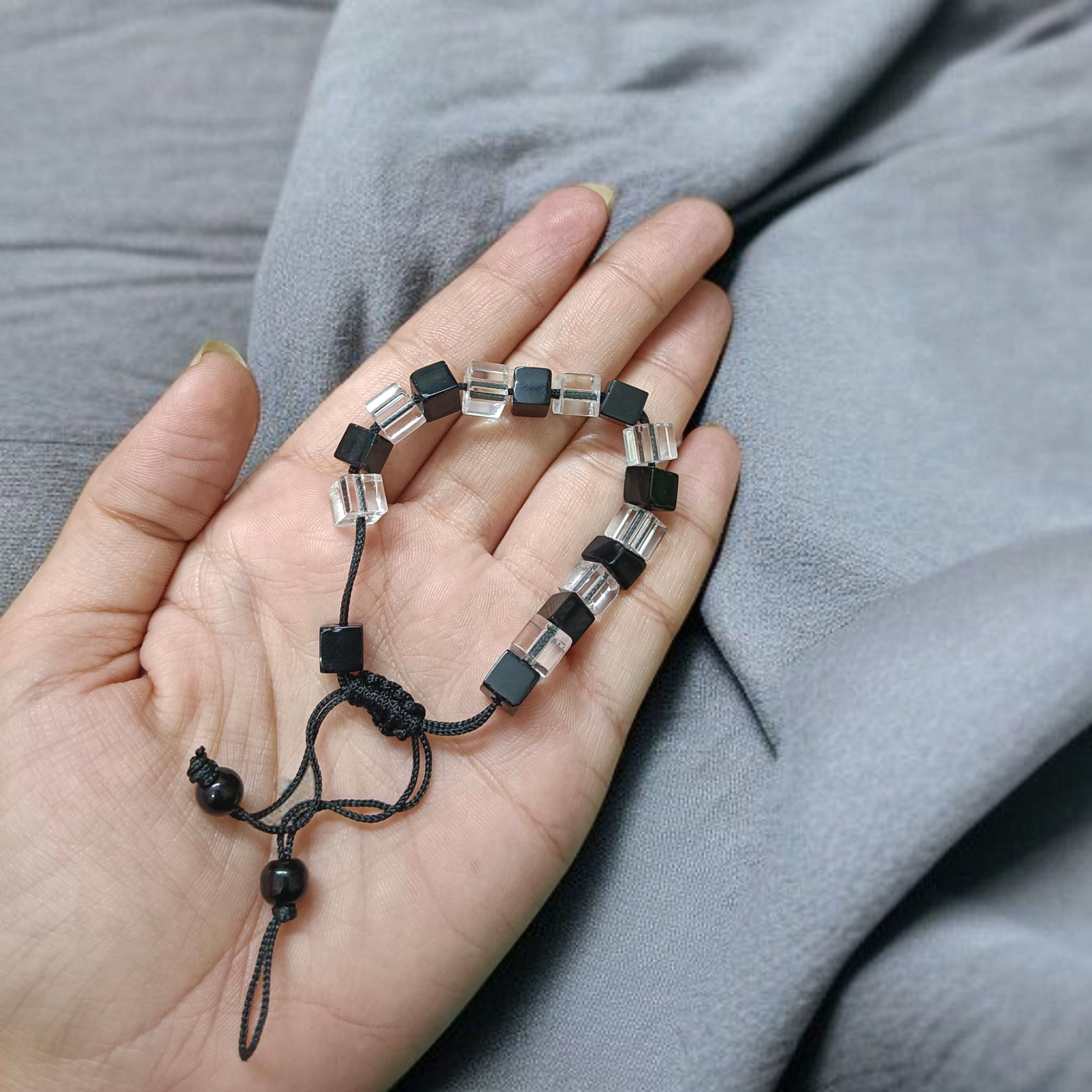 Black and white crystal bracelet with an evil eye symbol, featuring an adjustable thread for a customizable fit, designed for attraction and protection.