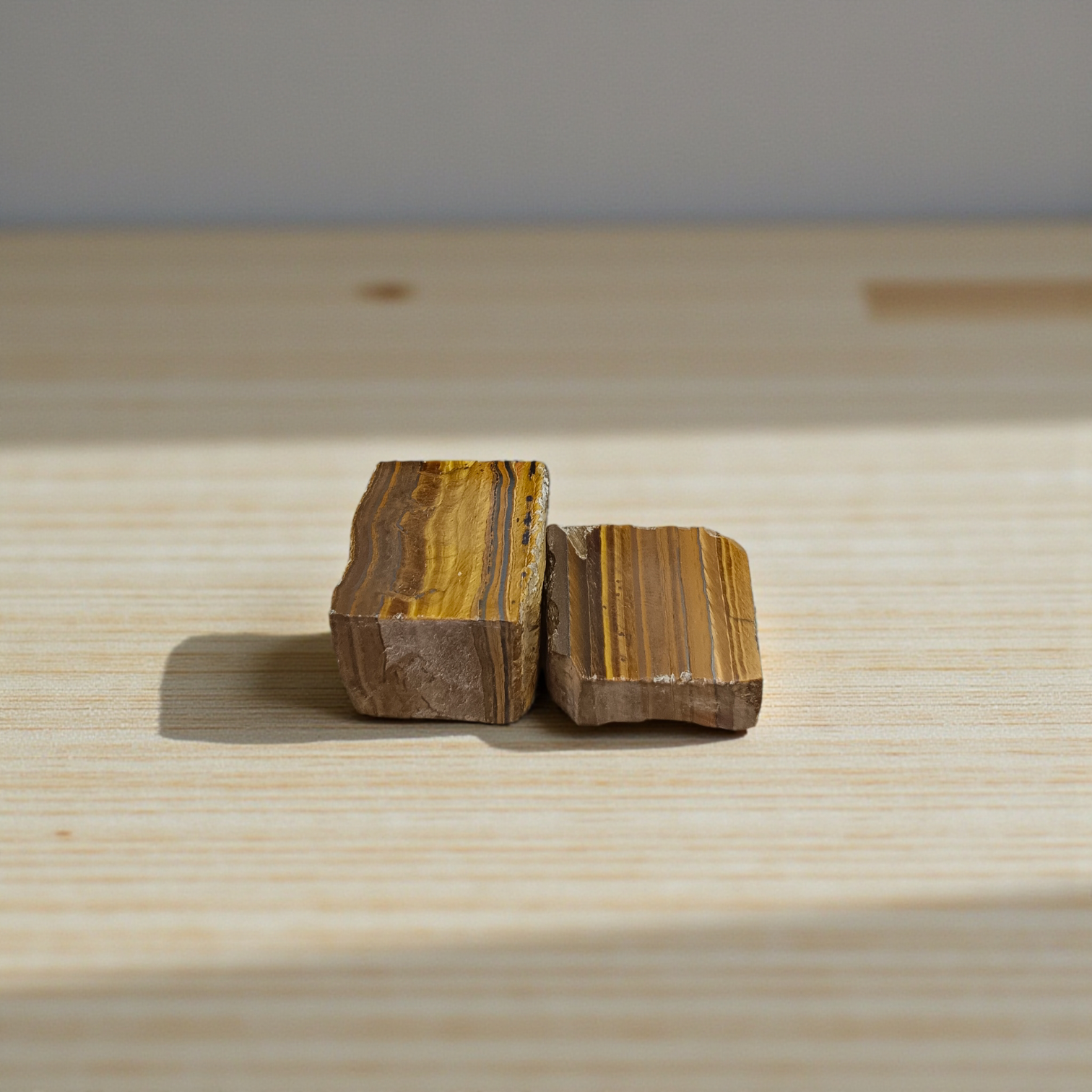 Two polished golden-brown Tiger Eye stones with smooth texture, placed side by side, reflecting natural shimmer and grounding energy
