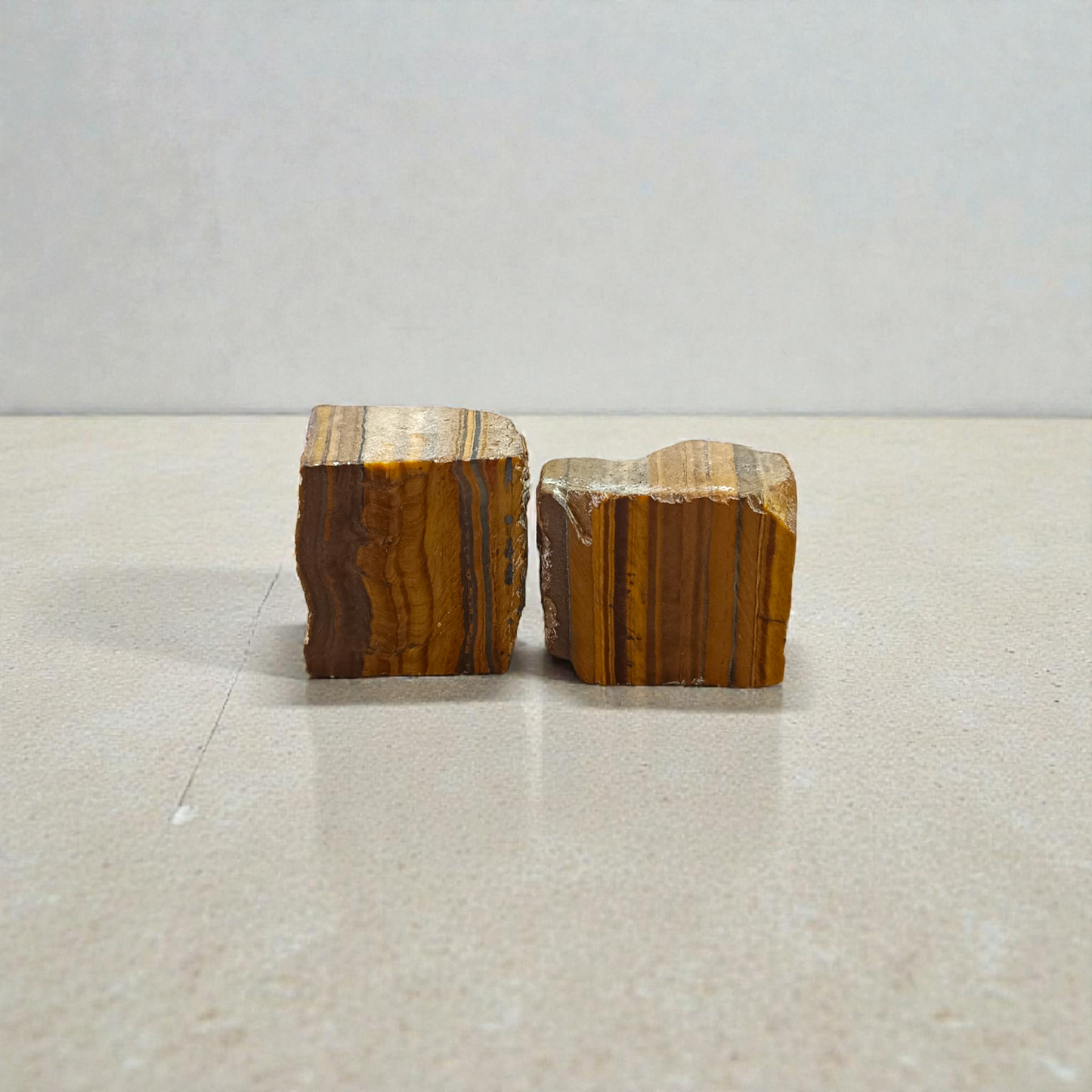 Two polished golden-brown Tiger Eye stones with smooth texture, placed side by side, reflecting natural shimmer and grounding energy