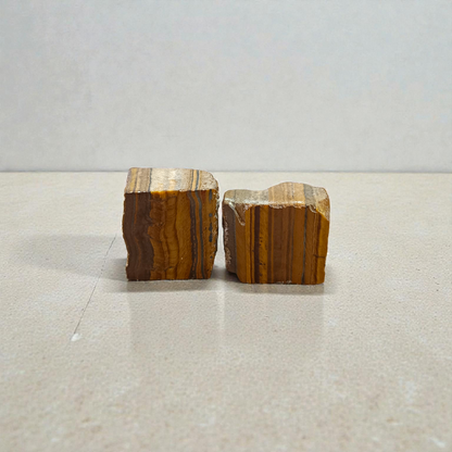 Two polished golden-brown Tiger Eye stones with smooth texture, placed side by side, reflecting natural shimmer and grounding energy